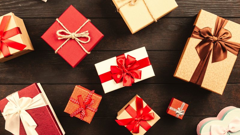 Photograph of wrapped gifts in several sizes, tied with red, white and brown ribbons, seen from above on a dark wooden table